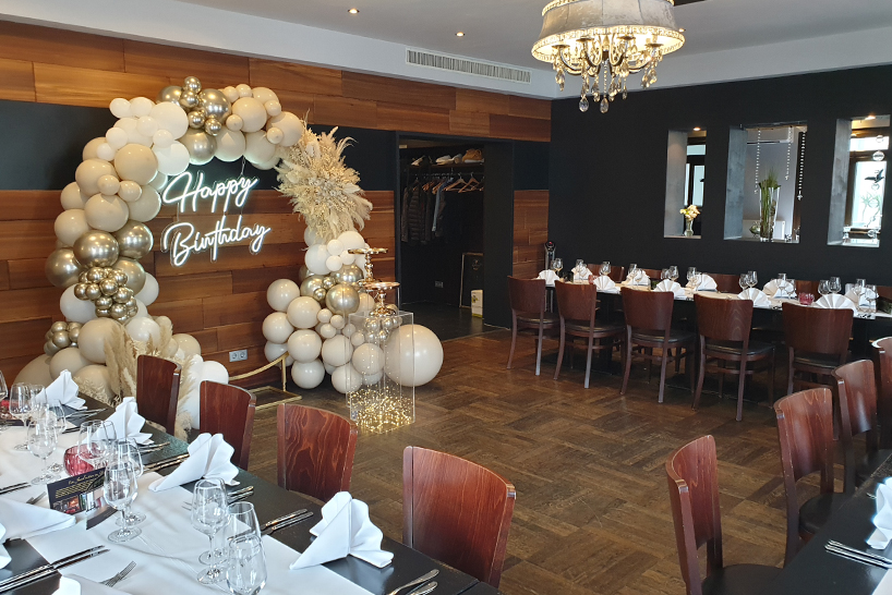 Elegante Geburtstagsdekoration mit Ballonbogen, „Happy Birthday“-Schriftzug in Neonfarben und Esstischen mit Servietten – perfekt für Ihre nächste Privatfeier oder einen besonderen Veranstaltungsort.