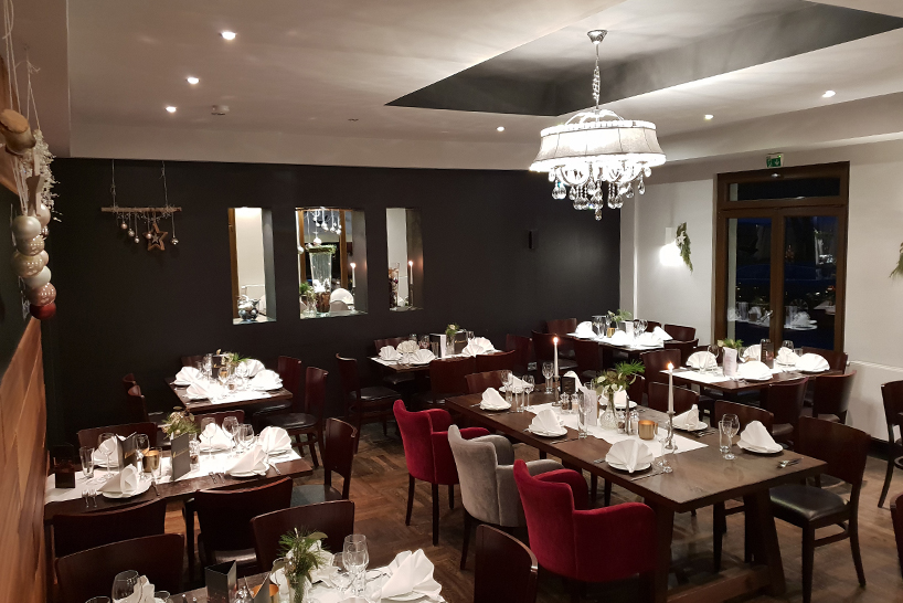 Ein eleganter Speisesaal mit gedeckten Tischen, weißen Servietten und einem Kronleuchter an der Decke – ein idealer Ort für Ihre Hochzeit oder Ihre private Feier.