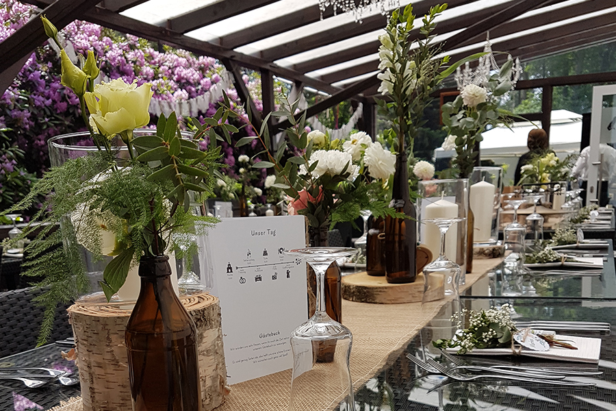 Elegantes Tischarrangement für eine Veranstaltung im Freien mit Blumen, Kerzen, Glasgeschirr und rustikalem Dekor – perfekt für Ihre nächste Feier an einer einzigartigen Hochzeits- oder Veranstaltungslocation, mit der Möglichkeit einer unvergesslichen Übernachtung für Ihre Gäste.
