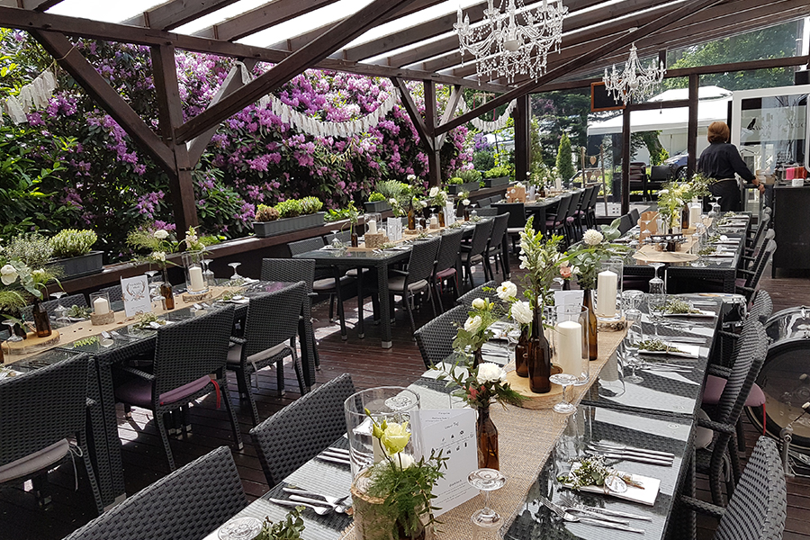 Elegante Veranstaltungslocation mit einem atemberaubenden Außenbereich zum Speisen, ausgestattet mit langen Tischen, Blumengestecken und Kronleuchtern unter einem Glasdach – ideal für Ihre nächste Privatfeier oder einen besonderen Anlass, mit der Möglichkeit einer Übernachtung.